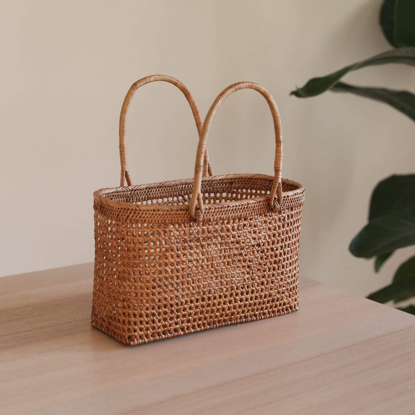 The Bali Rattan Woven Handbag handmade by Ganapati Crafts Co. in Bali is sitting a wood table looking stylish