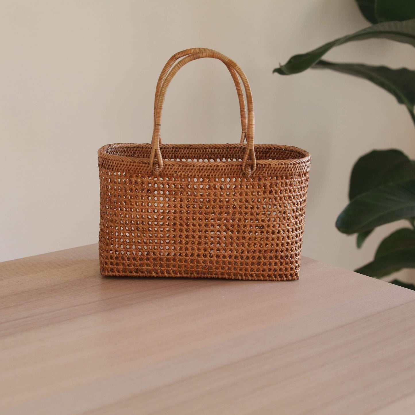 The Bali Rattan Woven Handbag handmade by Ganapati Crafts Co. in Bali is sitting a wood table looking stylish