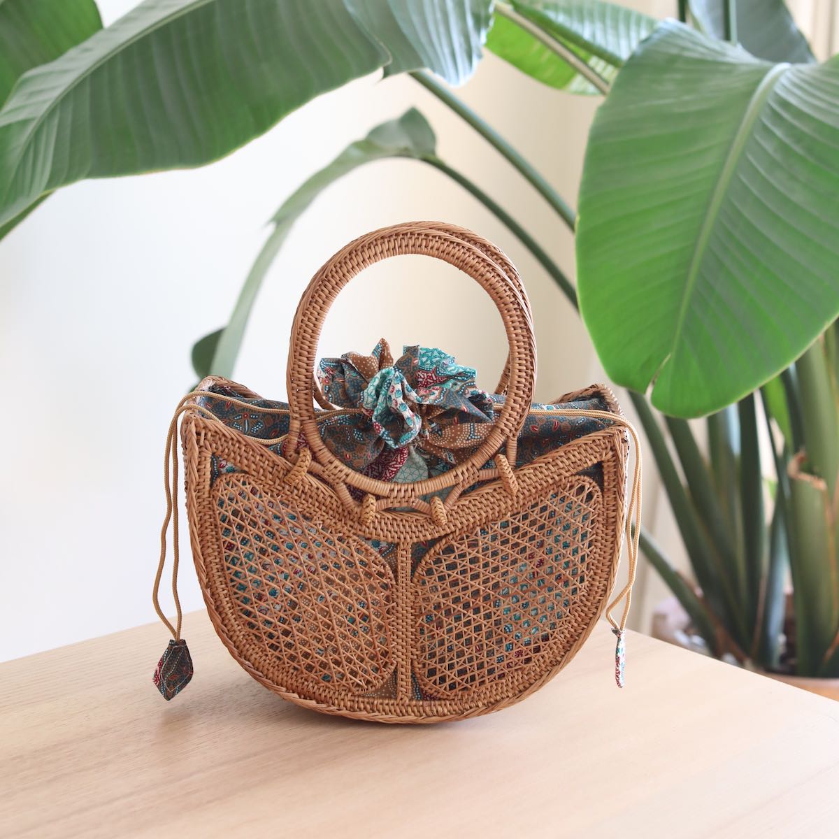 The Tulip Bali Rattan Clutch handmade by Ganapati Crafts Co. in Bali where all the Bali Rattan Bags are made is sitting on a wood table looking stylish