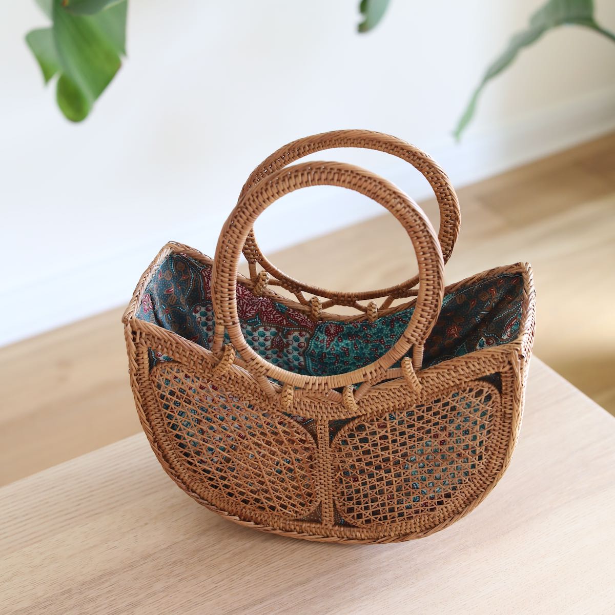 The Tulip Bali Rattan Clutch handmade by Ganapati Crafts Co. in Bali where all the Bali Rattan Bags are made is sitting on a wood table looking stylish