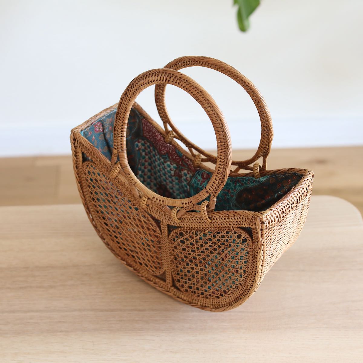 The Tulip Bali Rattan Clutch handmade by Ganapati Crafts Co. in Bali where all the Bali Rattan Bags are made is sitting on a wood table looking stylish