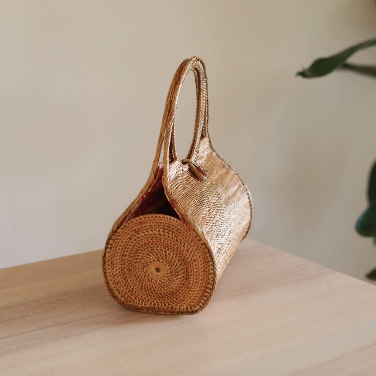 Bali Rattan Wheel Handbag handmade by Ganapati Crafts Co. in Bali is sitting on a wood table looking very stylish