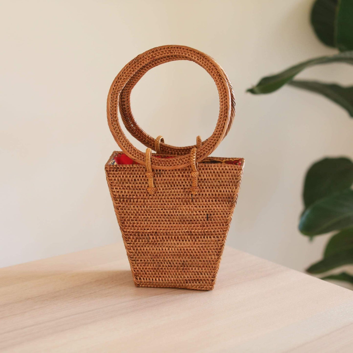 The Bali Trapezoid Rattan Handbag handmade by Ganapati Crafts Co. in Bali is sitting on a wood table