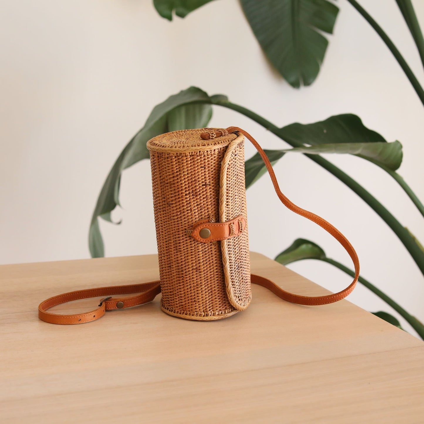 A Turbo Bag in Bali Rattan Crossbody Bag collection by Ganapati Crafts Co. handwoven in Bali is sitting on a wood table