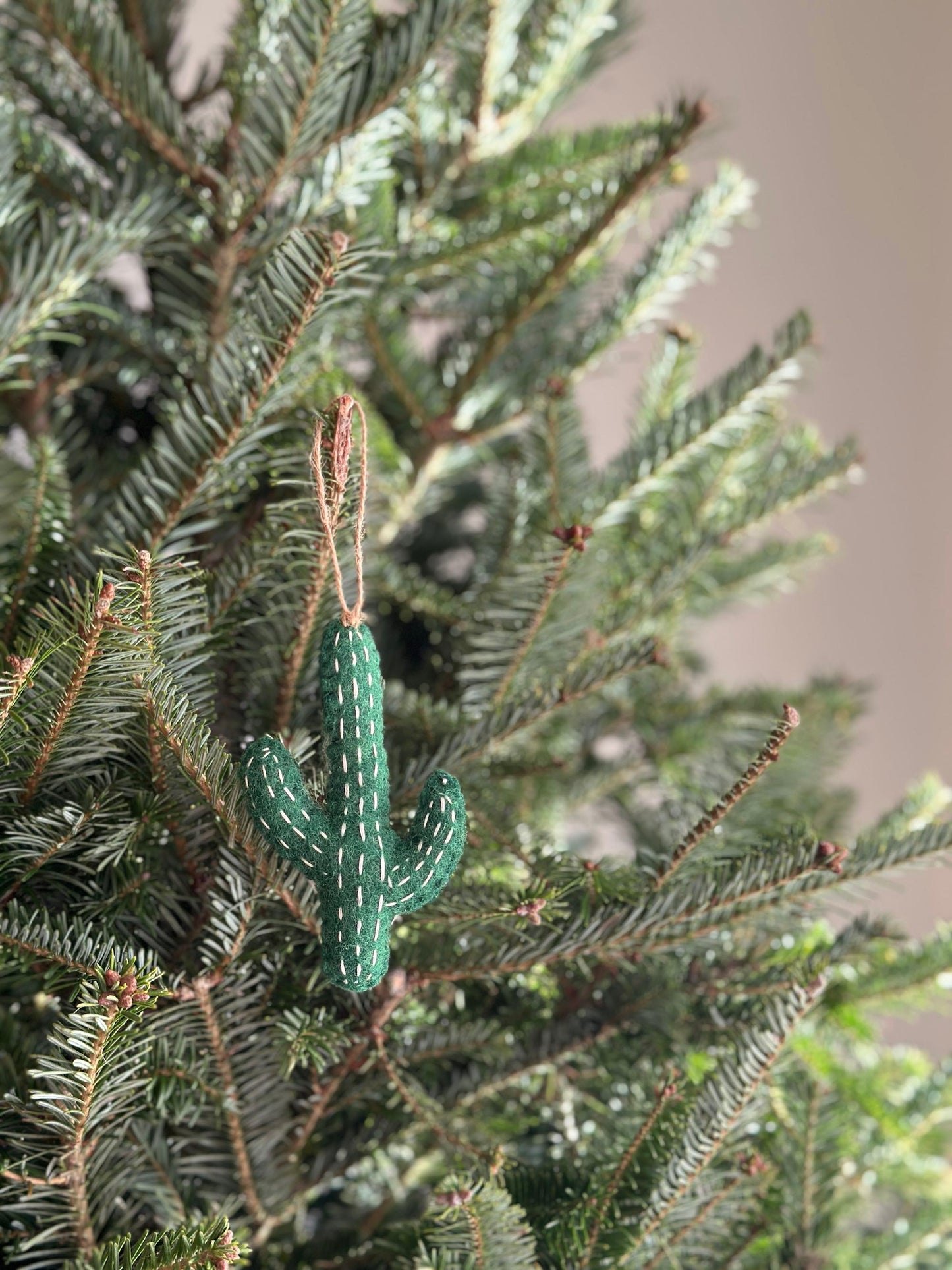 A handmade felt cactus ornaments by Deer Harbour Design hanging on a Christmas tree