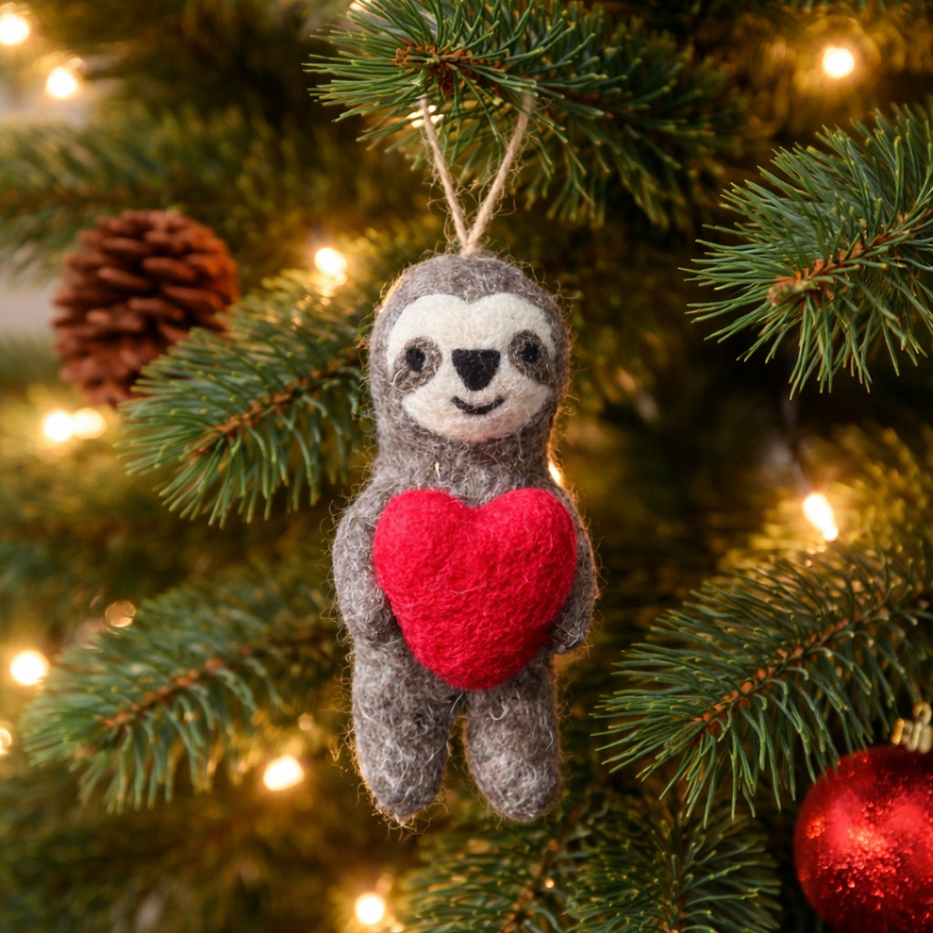 Sloth ornament with a red heart hanging on a Christmas tree.
