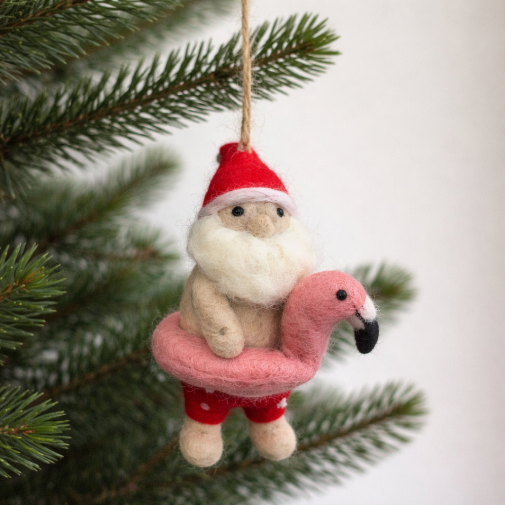 Decorative wool felt ornament of a Santa Claus with a flamingo swim ring and Christmas tree in the background