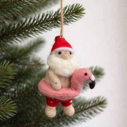 Decorative wool felt ornament of a Santa Claus with a flamingo swim ring and Christmas tree in the background