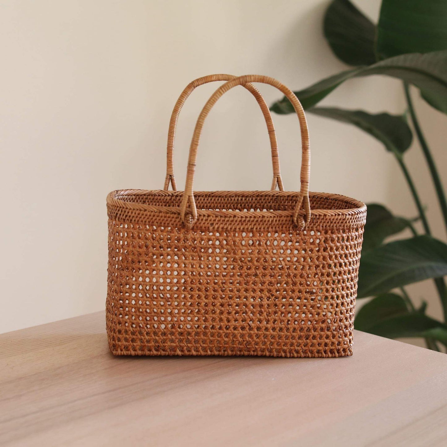 The Bali Rattan Woven Handbag handmade by Ganapati Crafts Co. in Bali is sitting a wood table looking stylish