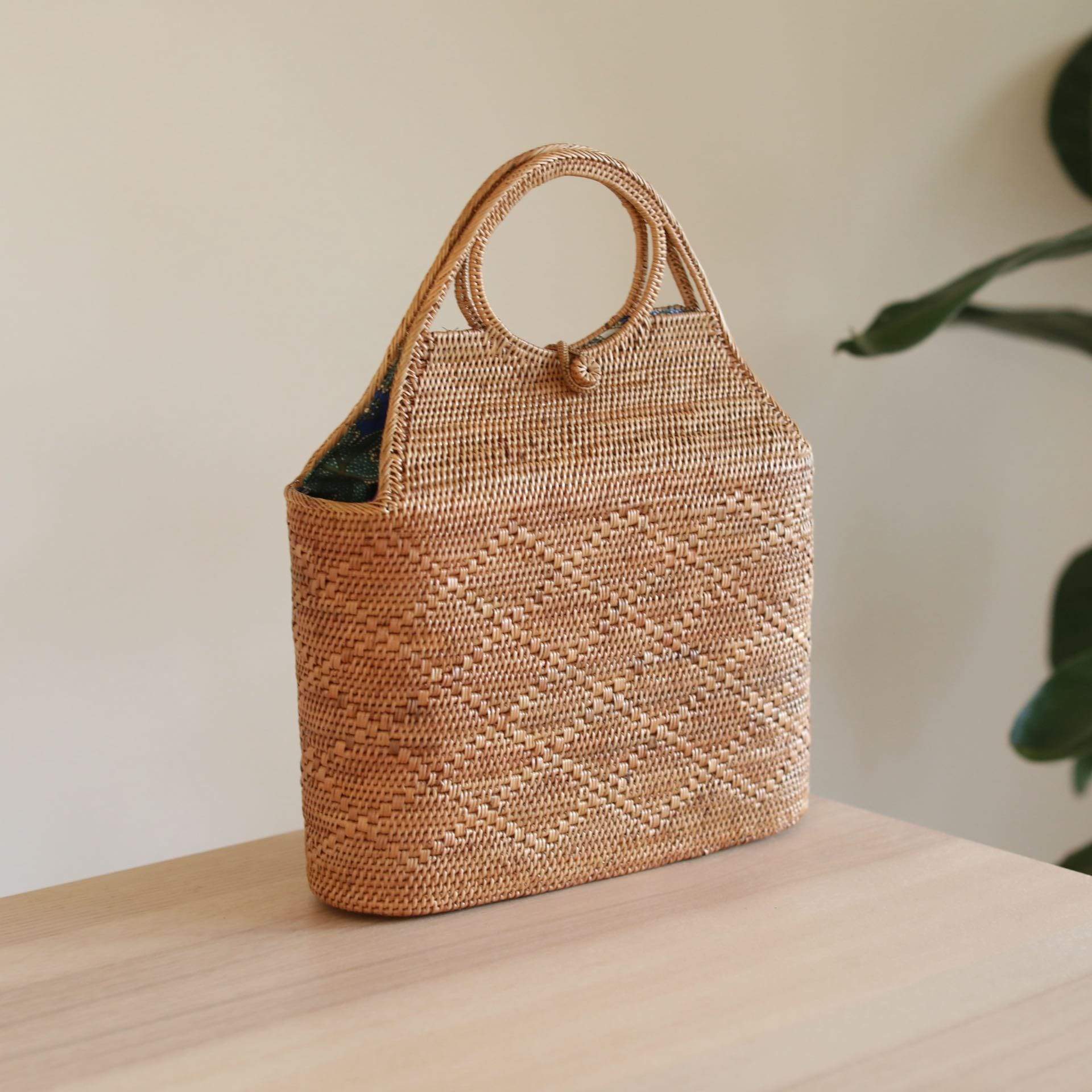 The Tall Malboro Bali Rattan Straw Handbag handmade by Ganapati Craft in Bali where all the Bali Rattan Straw Bags are made is sitting on a table looking stylish