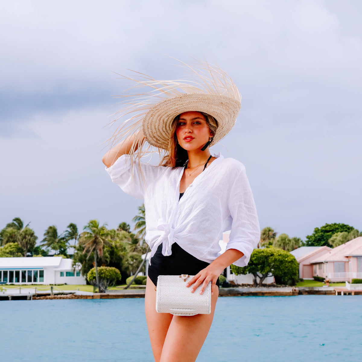 a female is holding a Bali Envelope Rattan Crossbody Bag handmade by Ganapati Crafts Co. in Bali taking picture creating a sense of luxury holidays