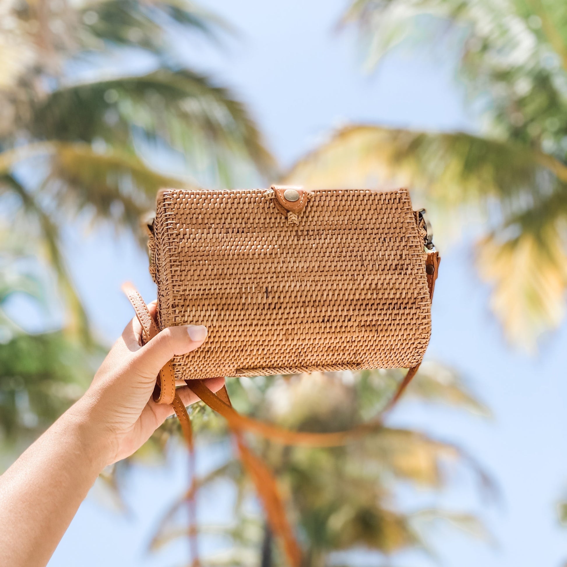 Bali Envelope Rattan Crossbody Bag handmade by Ganapati Crafts Co. in Bali sitting on a wood table with sun coming from the window creating a sense of luxury holidays