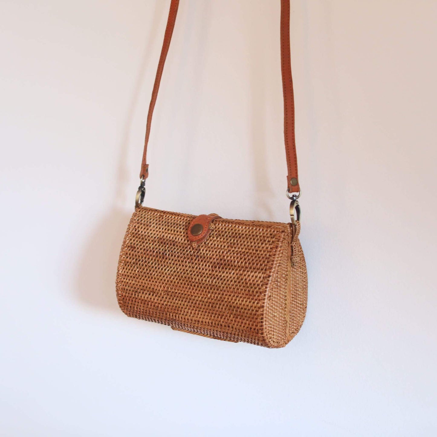 Bali Envelope Rattan Crossbody Bag handmade by Ganapati Crafts Co. in Bali sitting on a wood table with sun coming from the window creating a sense of luxury holidays