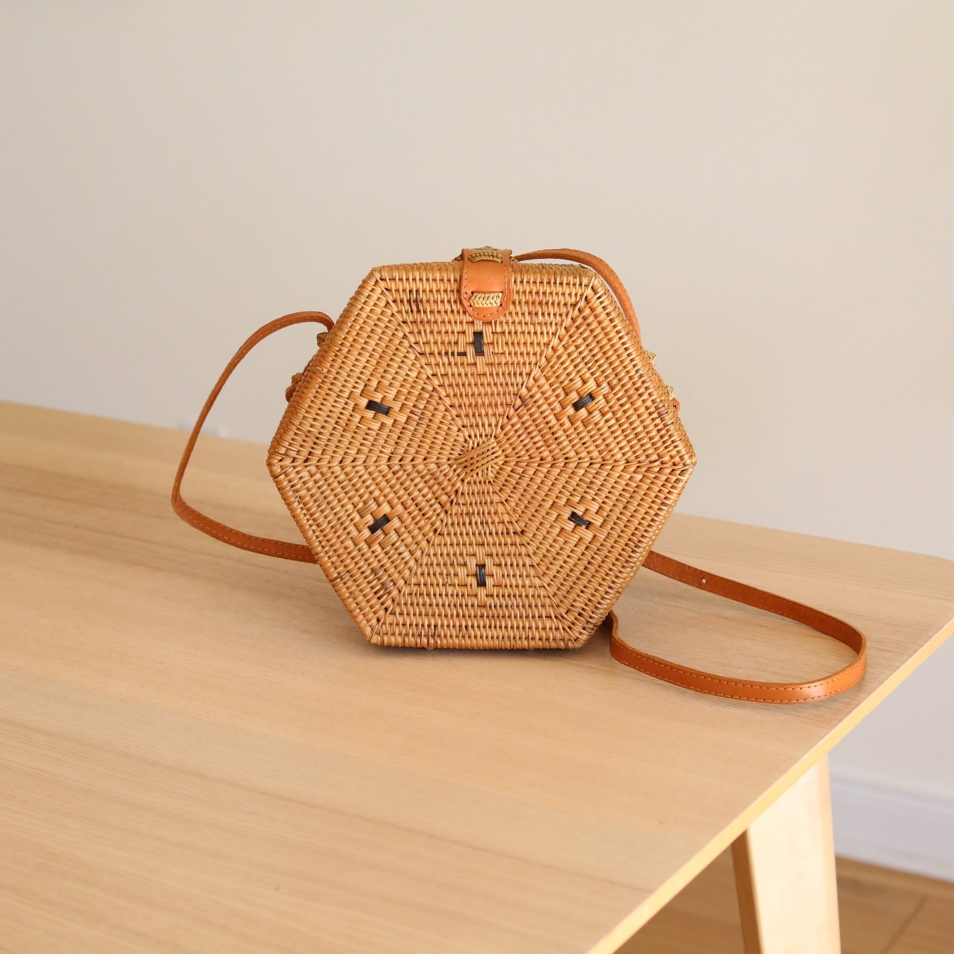 Bali Hexagon Rattan Crossbody Bag by Ganapati Crafts Co. handwoven by skilled artisans in Bali is sitting on a wood table