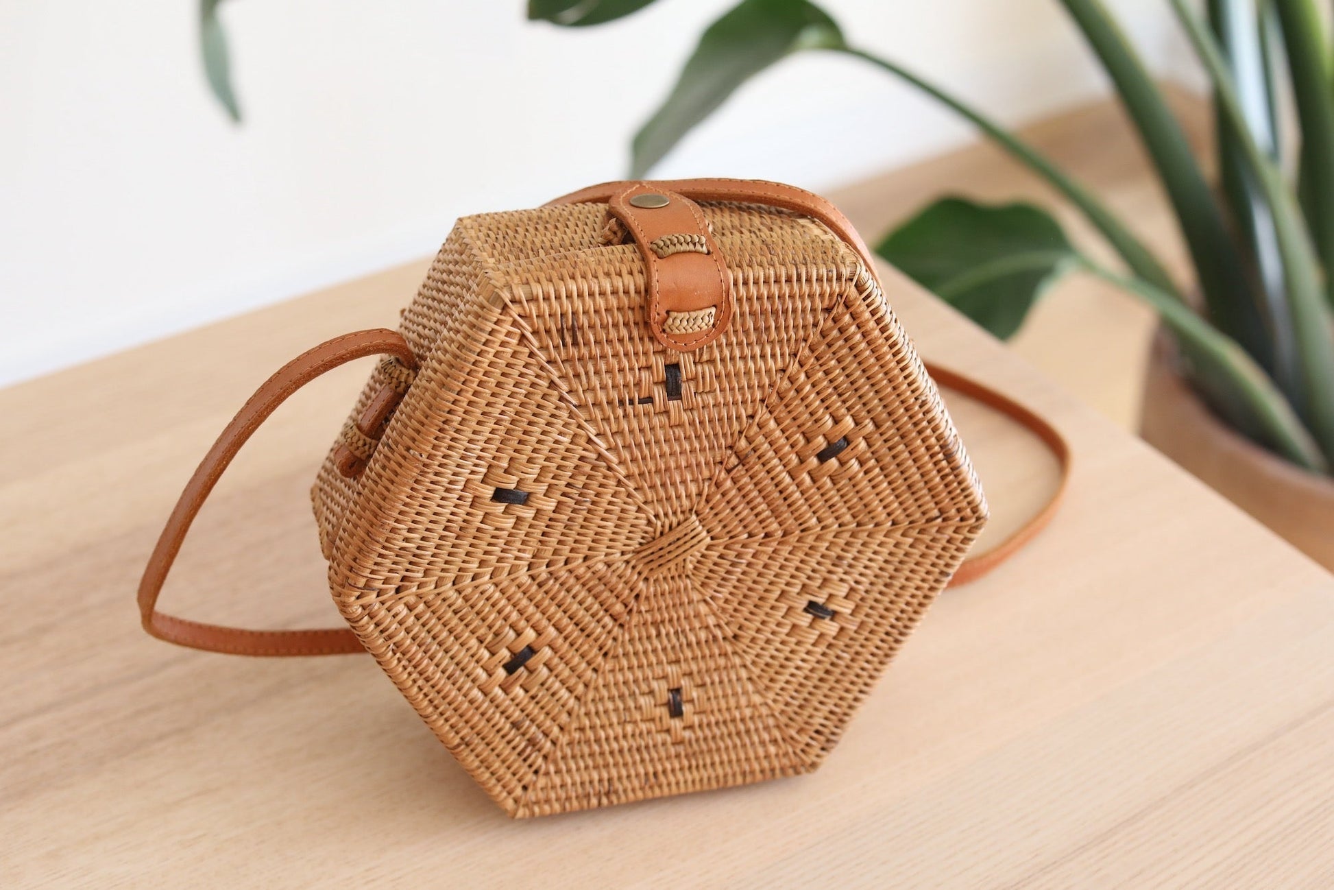 Bali Hexagon Rattan Crossbody Bag by Ganapati Crafts Co. handwoven by skilled artisans in Bali is sitting on a wood table