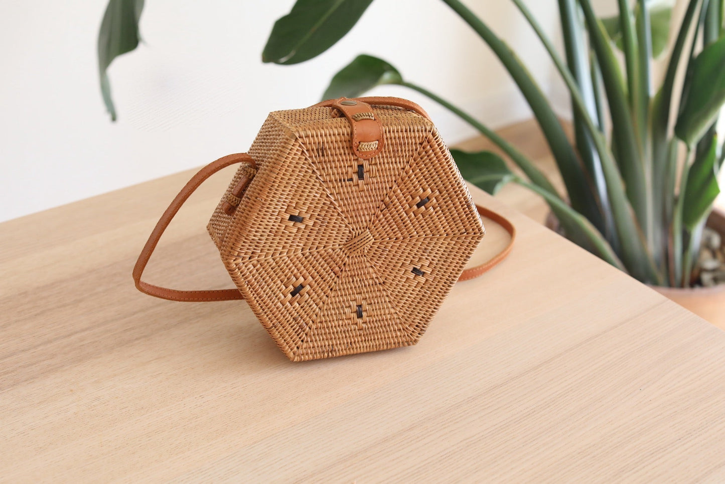 Bali Hexagon Rattan Crossbody Bag by Ganapati Crafts Co. handwoven by skilled artisans in Bali is sitting on a wood table