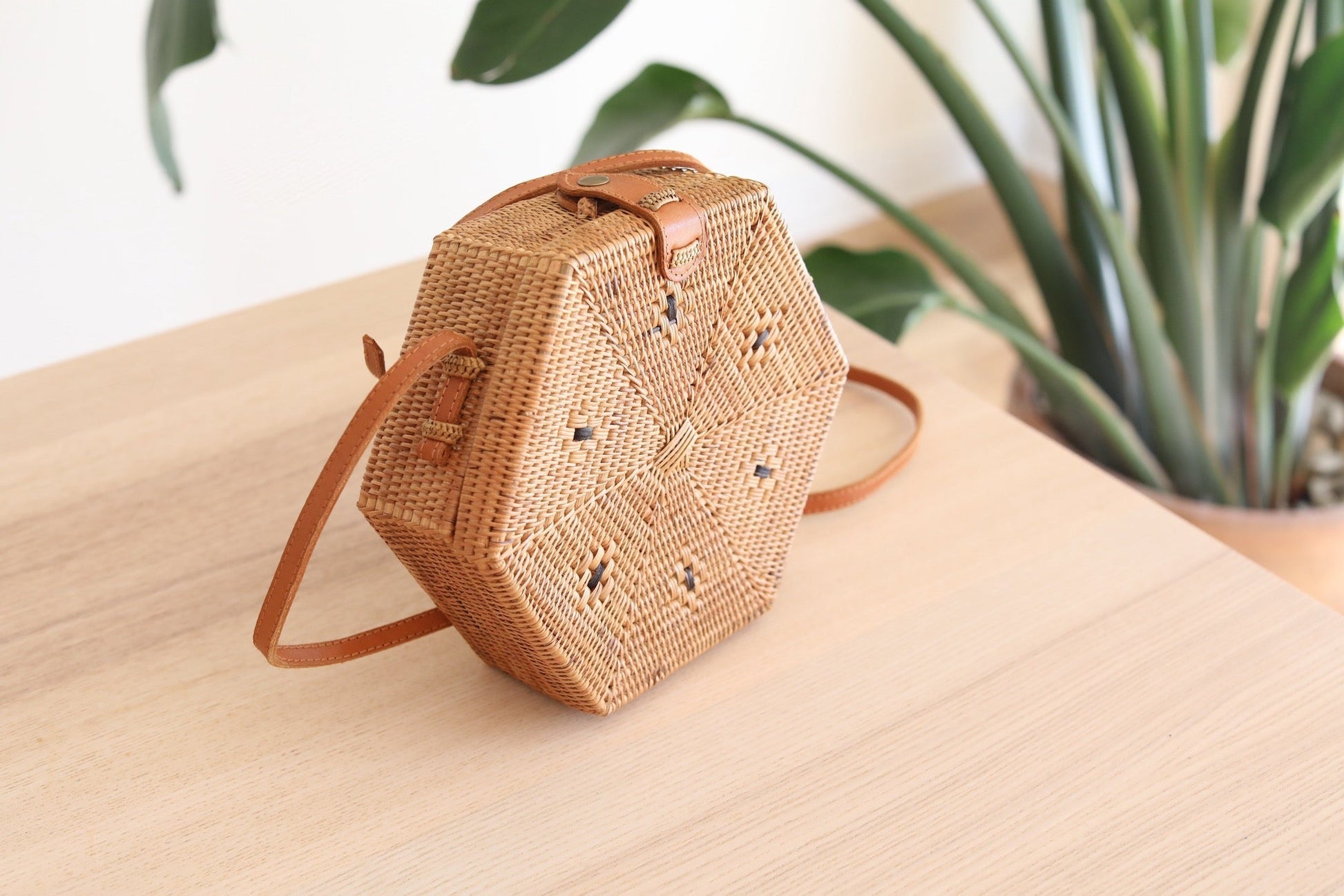 Bali Hexagon Rattan Crossbody Bag by Ganapati Crafts Co. handwoven by skilled artisans in Bali is sitting on a wood table