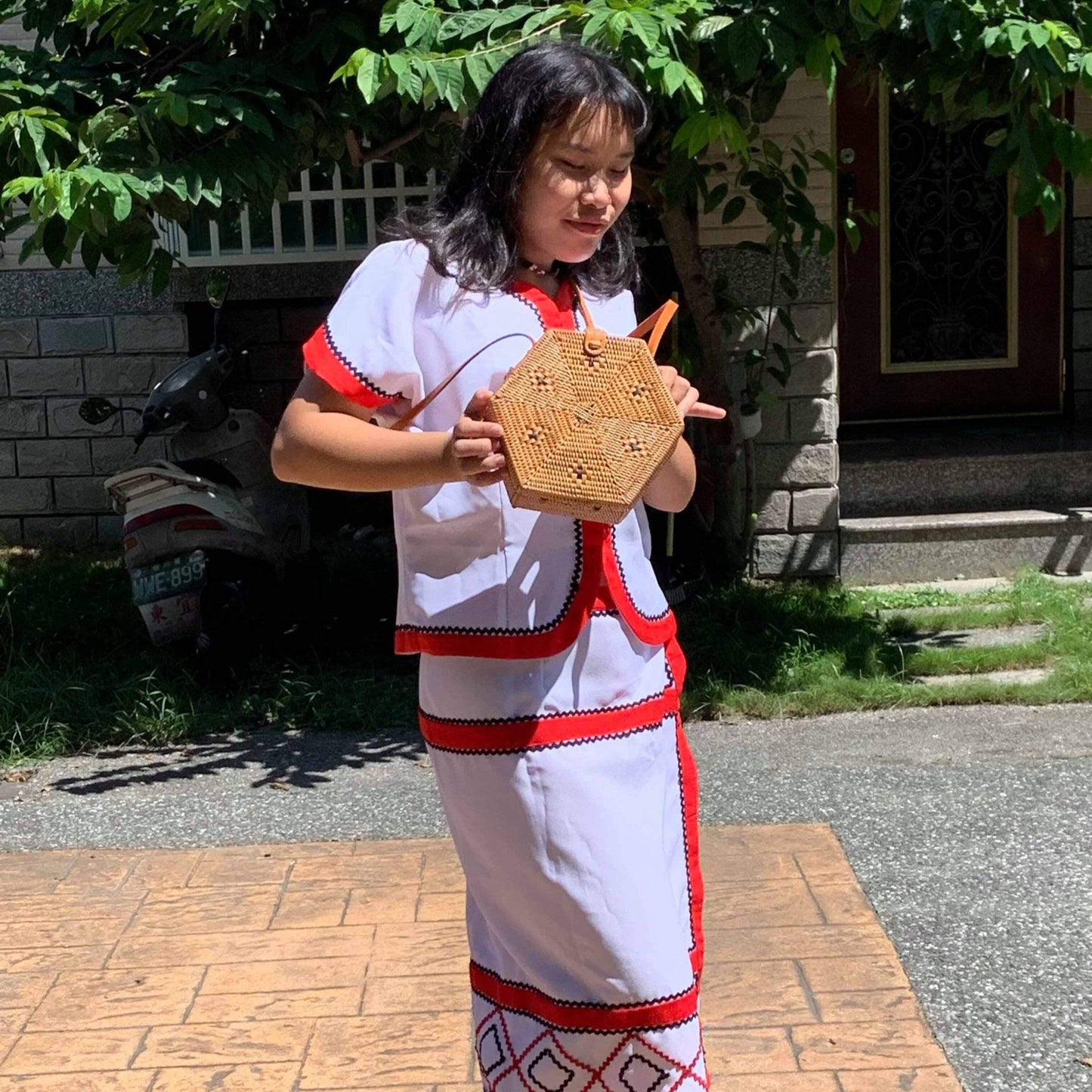 A female dressing in Bali traditional dress is holding a Bali Hexagon Rattan Crossbody Bag by Ganapati Crafts Co. handwoven by skilled artisans in Bali