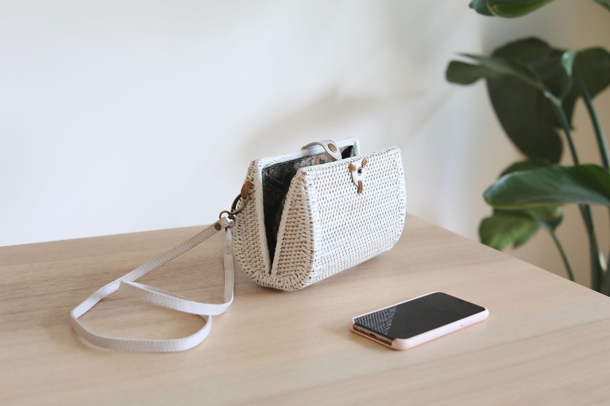 Bali Envelope Rattan Crossbody Bag handmade by Ganapati Crafts Co. in Bali sitting on a wood table with sun coming from the window creating a sense of luxury holidays